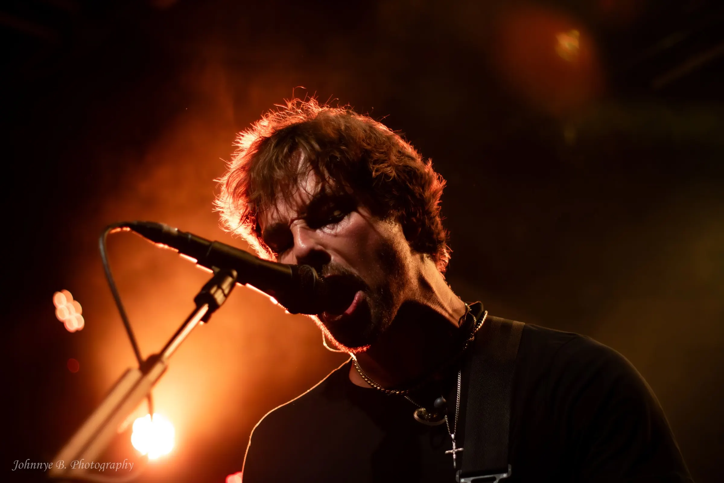 Vocalist leaning into the microphone under red stage light, backlit by the rig
