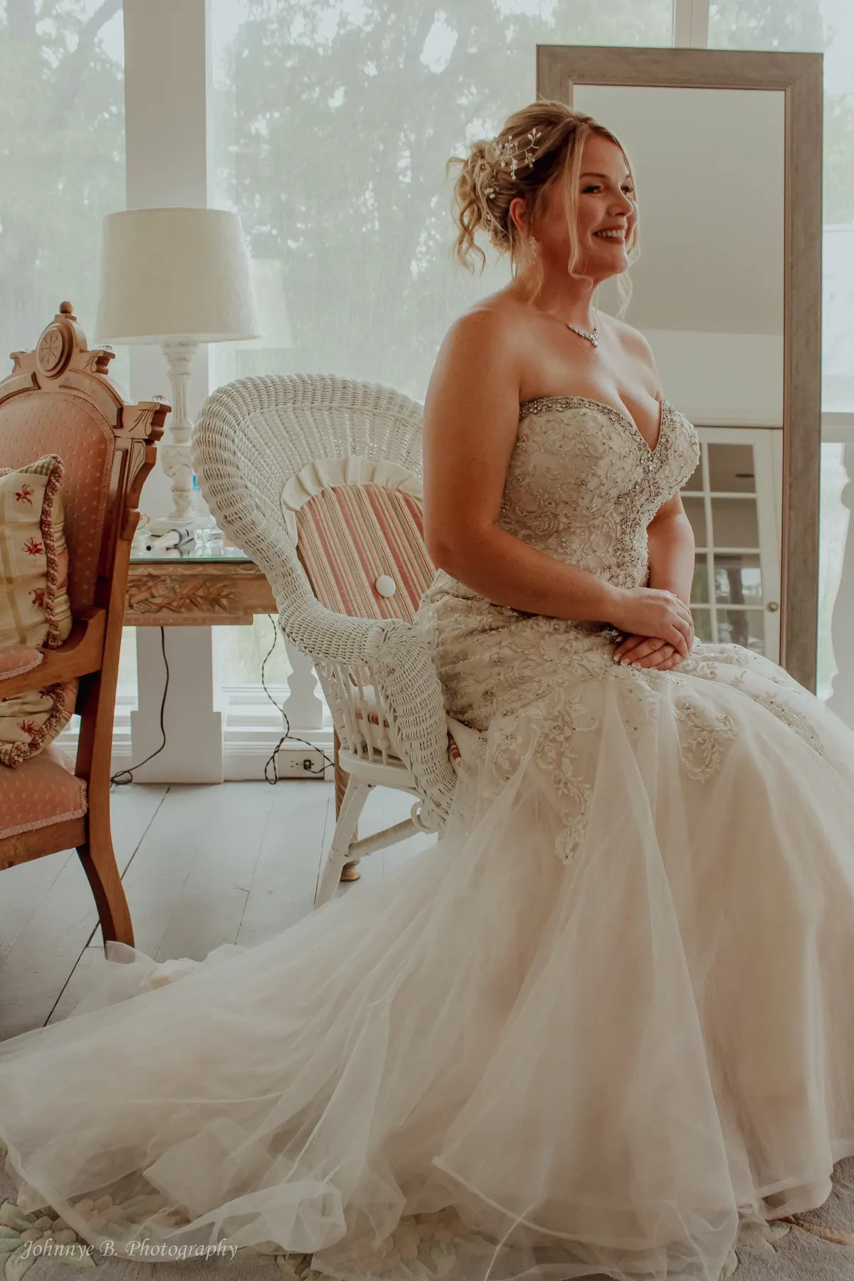 Bride seated by a window in a beaded gown, laughing