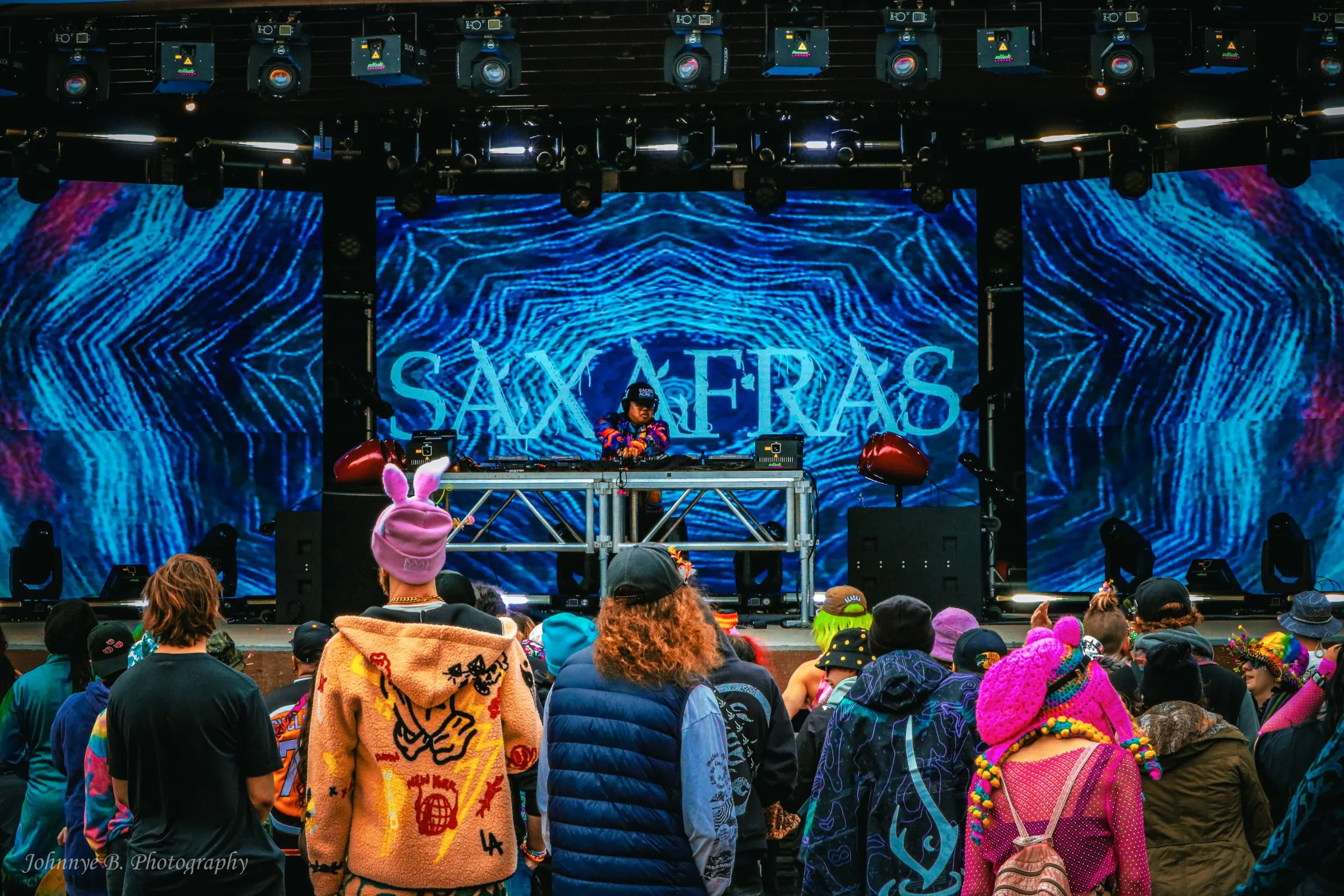 Crowd in festival colours watching a DJ on the Saxafras stage, blue projection behind